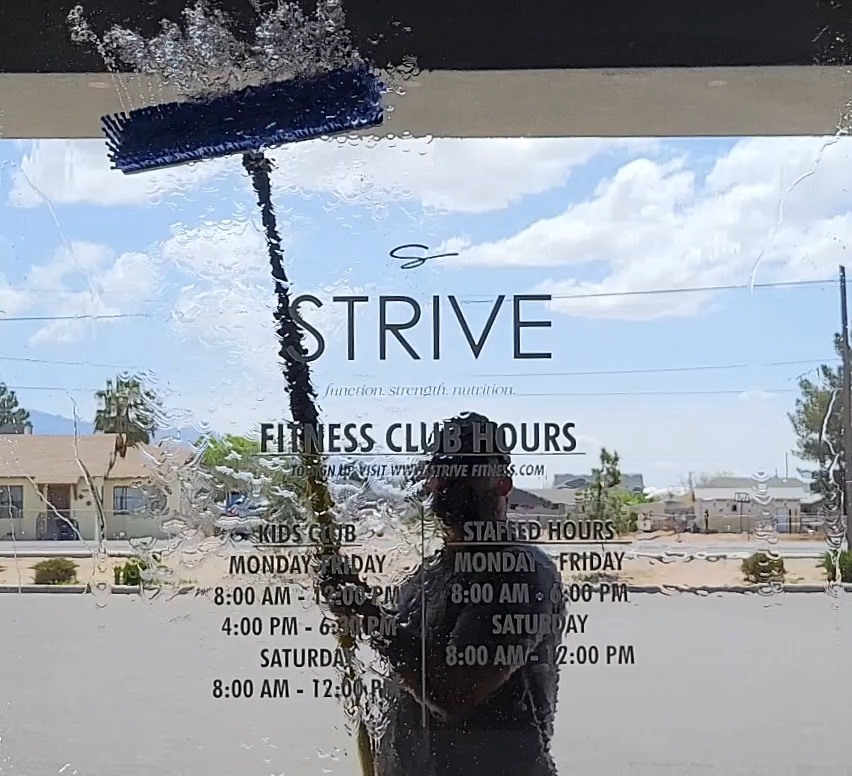 Up Top cleaning the front glass at Strive Fitness Club, with the Strive sign clearly visible